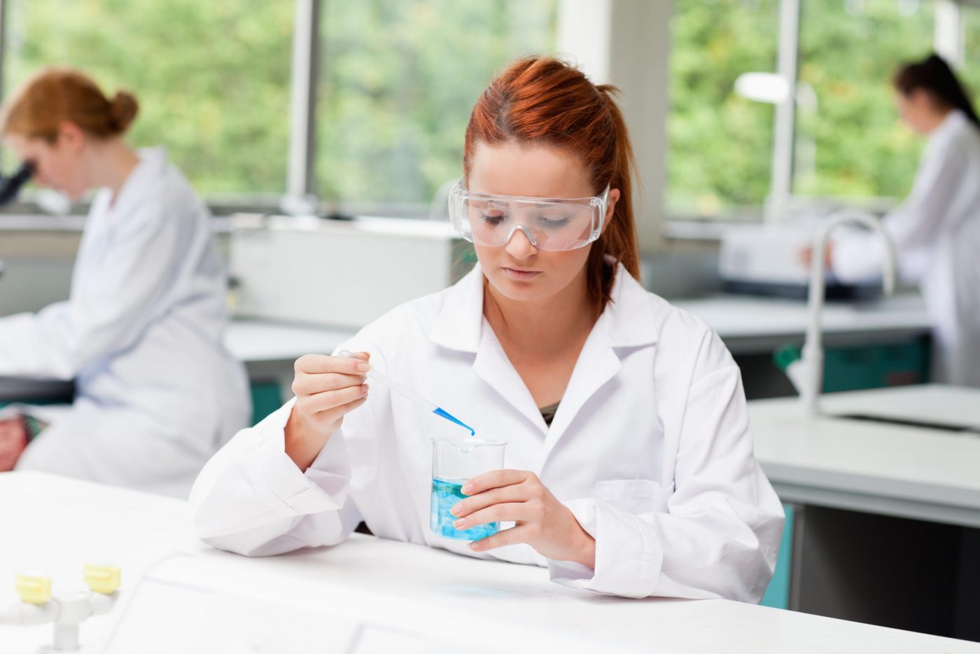 Science student dropping liquid in a beaker while her classmates are working