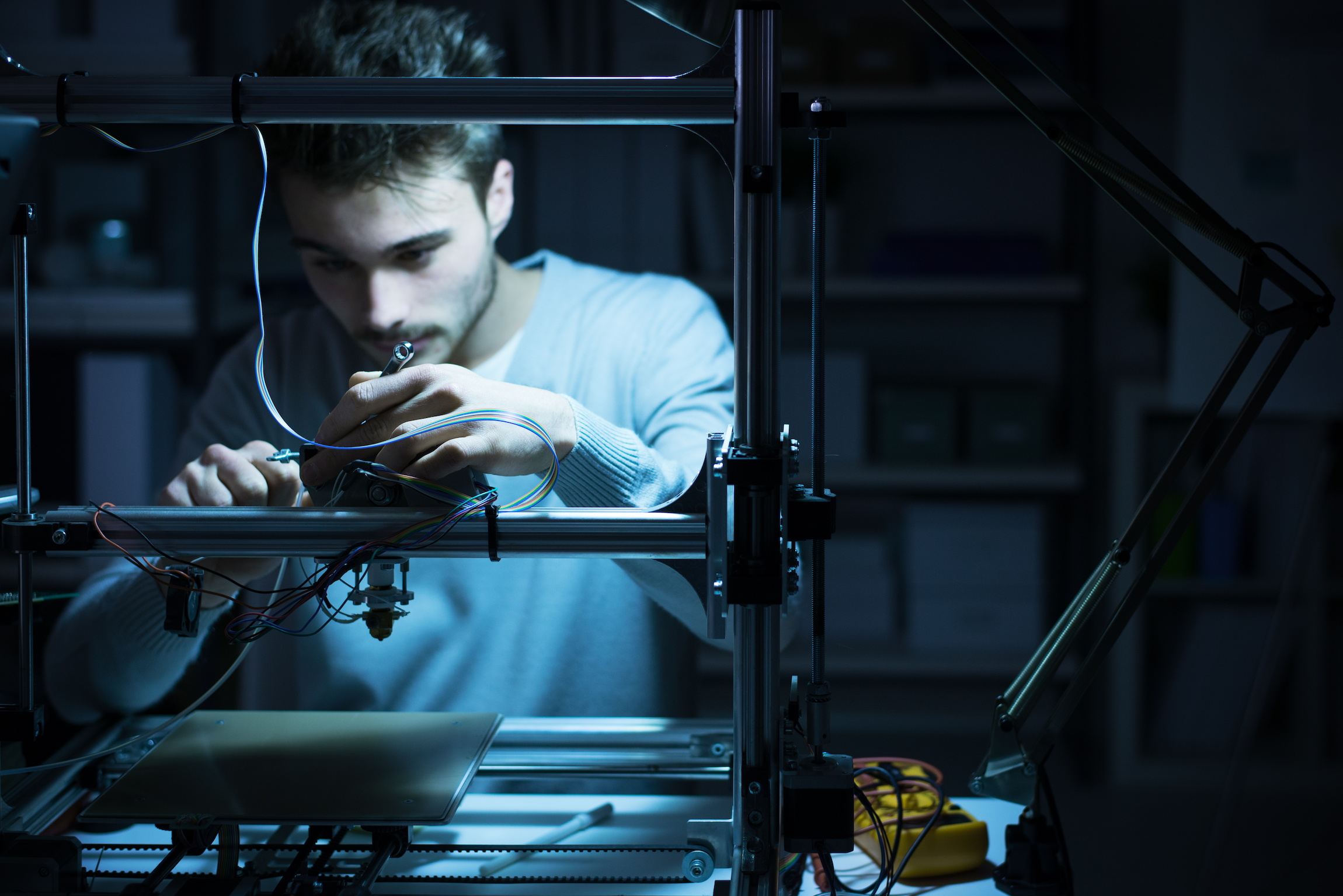 Young engineer working at night in the lab, he is adjusting a 3D printer's components, technology and engineering concept