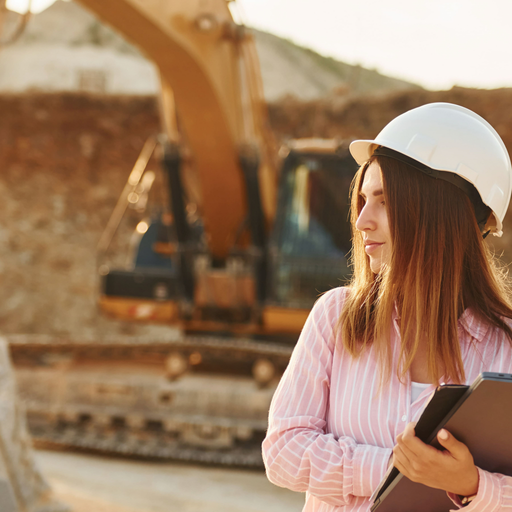 Female construction worker wearing a hard hat on a site with a digger in the background